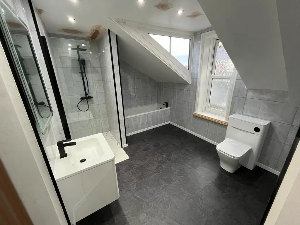 After: rebuilt attic bathroom with bath below the dormer, matt black shower and slate-effect floor