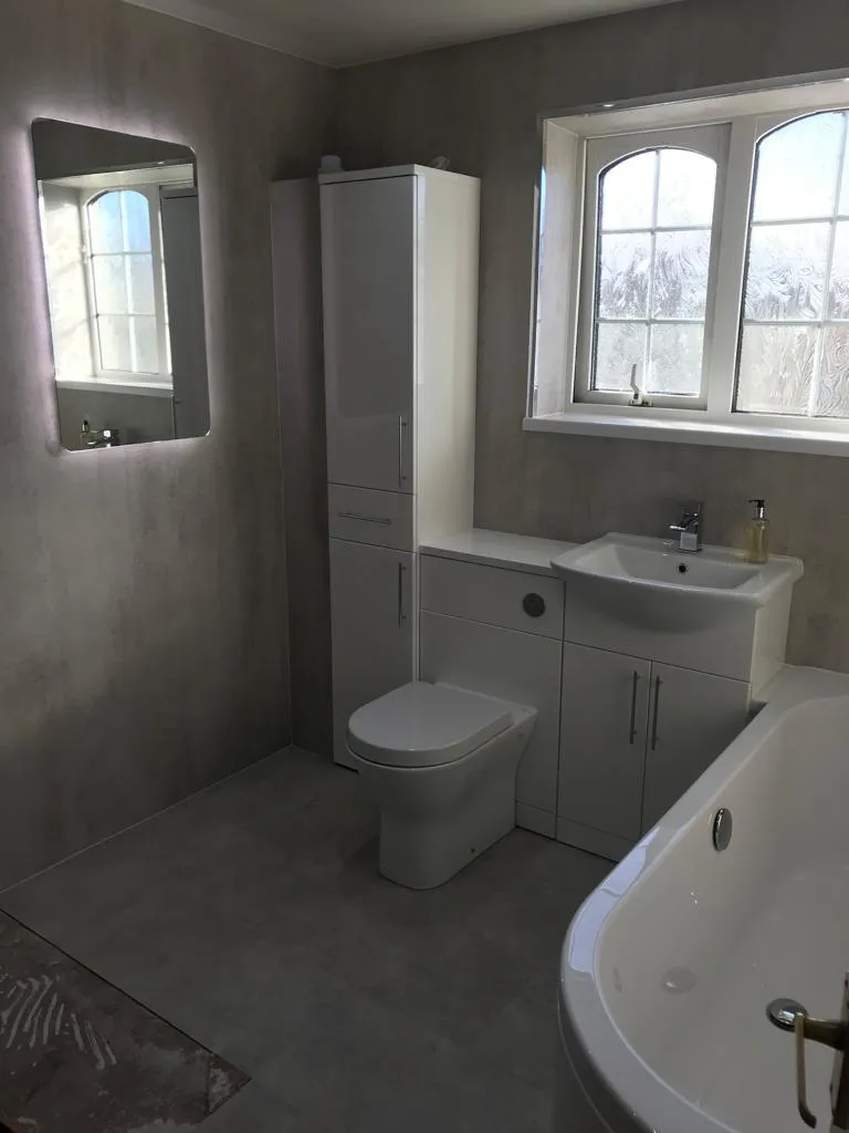 Bathroom with concrete-effect walls, white gloss furniture, backlit mirror and arched leaded windows