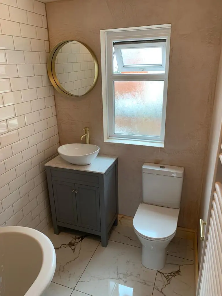 Countertop basin on a grey vanity with tall brass tap and round brass-framed mirror