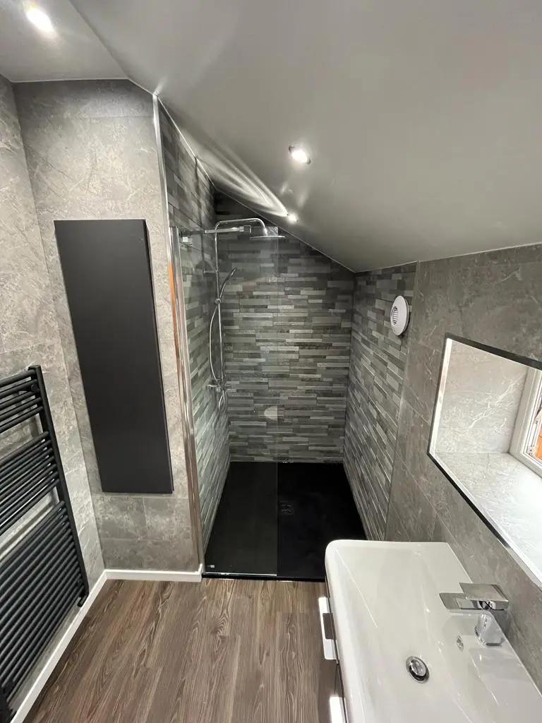 Shower under the sloped loft ceiling with stone-strip feature tiles and black wall panel