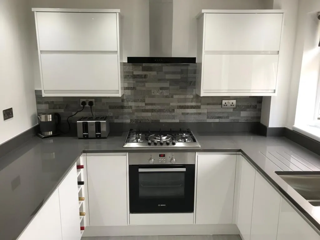 White gloss handleless kitchen with grey quartz, slate-strip splashback and gas hob